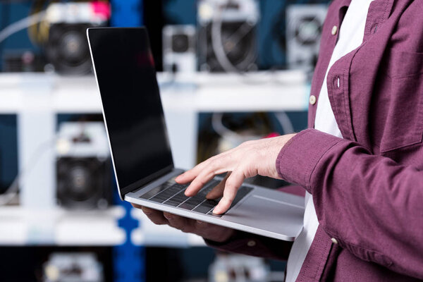 cropped shot of computer engineer working with laptop at cryptocurrency mining farm