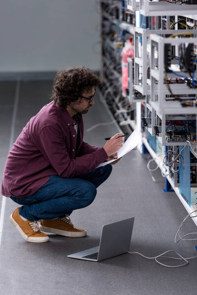 serious computer engineer working while sitting on floor at cryptocurrency mining farm