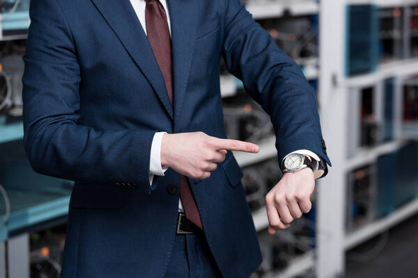 cropped shot of businessman pointing at wristwatch at ethereum mining farm