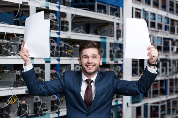 successful young businessman with papers celebrating victory at cryptocurrency mining farm