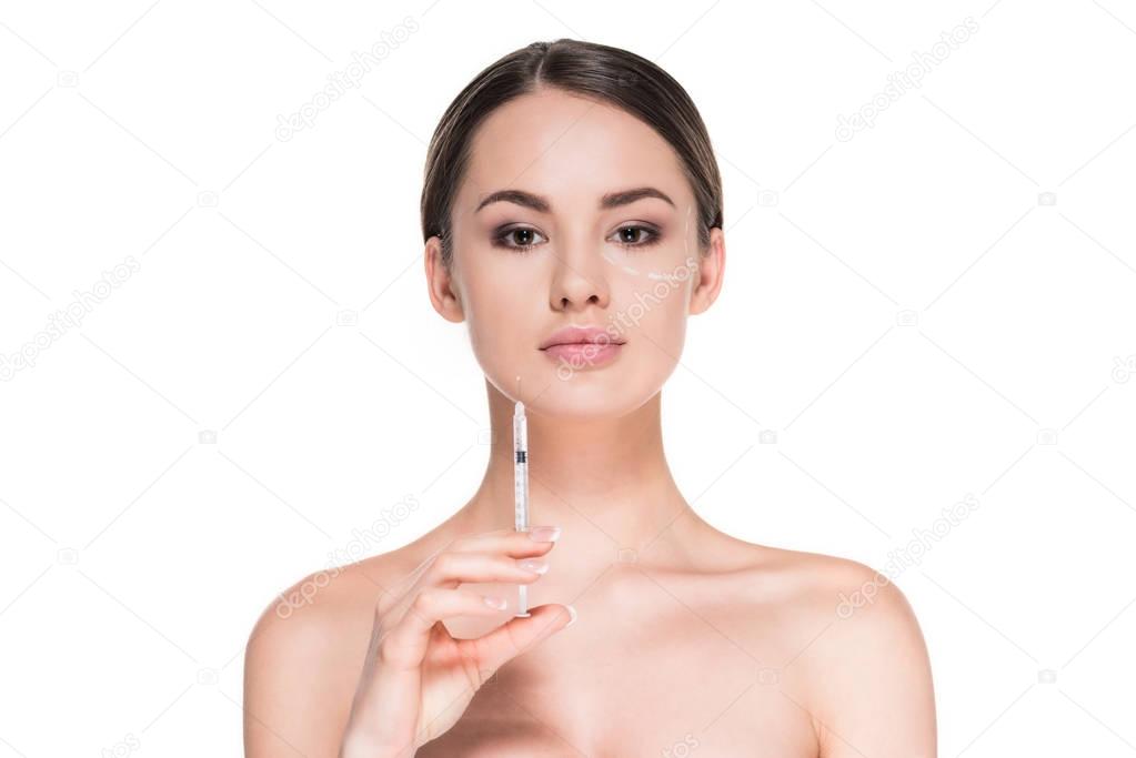 attractive young woman with dotted line drawn on face for plastic surgery holding syringe isolated on white