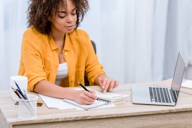 laptop ile çalışma ve not defterinde yazılı güzel genç kadın