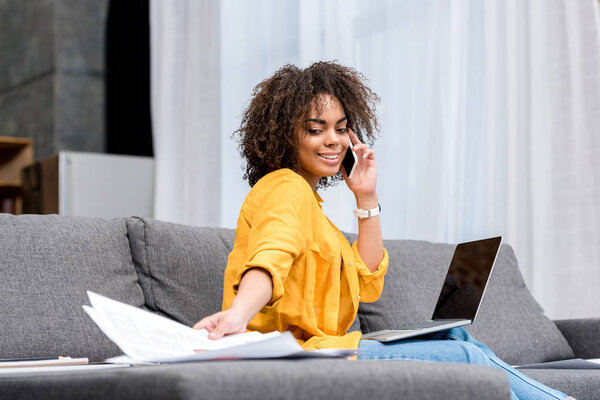 happy young woman working and talking by phone at home on couch