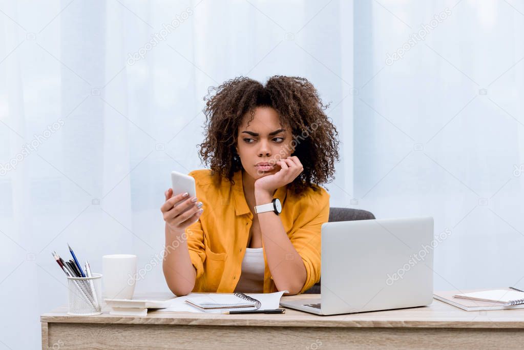 suspecting young woman looking at smartphone at workplace