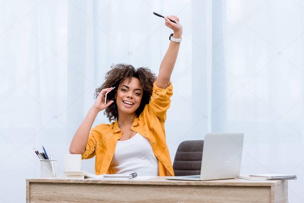 beautiful young woman talking by phone and raising hand happily