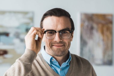 Smiling adult man fixing his eyeglasses clipart