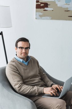 Sandalyede oturan ve dizüstü bilgisayarda çalışma gözlüklü adam
