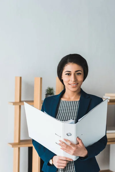 Smiling businesswoman holding folder in modern office