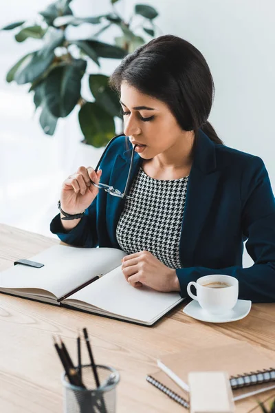 Jovem Empresária Olhando Para Notepad Segurando Vidro Por Mesa — Fotografia de Stock