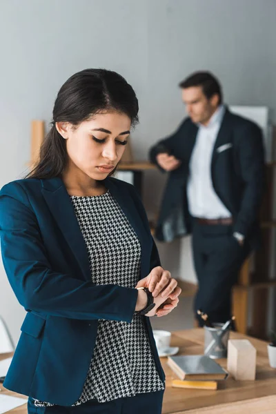 Businesswoman Controllo Orologio Mentre Uomo Abito Lavoro Piedi Scaffali Ufficio — Foto stock gratuita