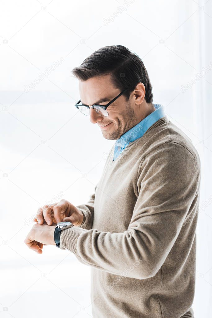 Attractive man wearing glasses checking his watch by window