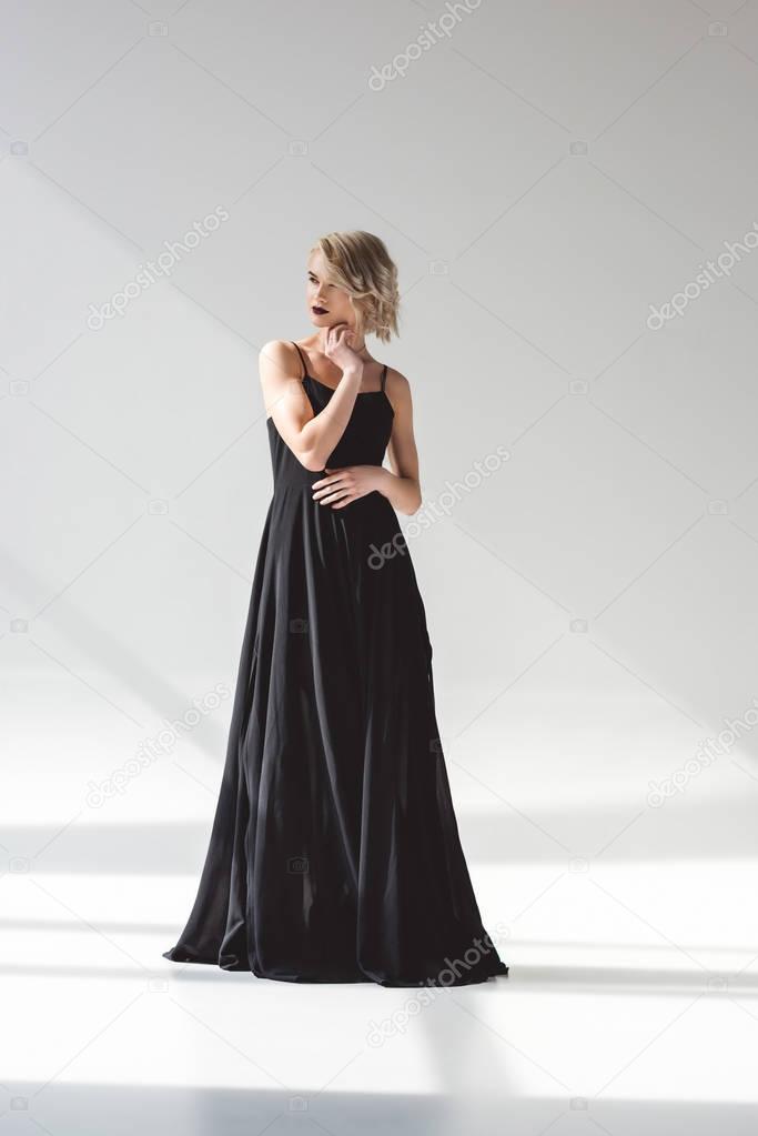 blonde young woman posing in elegant black dress, on grey 