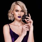 Blonde girl posing in fashionable purple dress with black rose, isolated on black