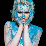 Young woman posing in blue powder paint, isolated on black