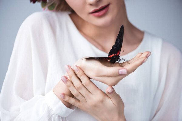 cropped view of girl with alive butterfly on hand, isolated on grey