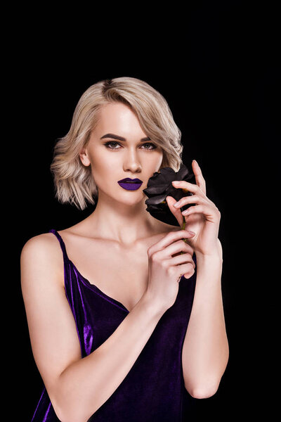 blonde girl posing in fashionable purple dress with black rose, isolated on black