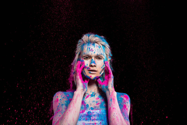 fashionable girl posing in pink and blue holi powder, isolated on black