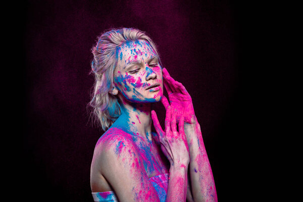 tender girl posing in pink and blue holi powder, isolated on black