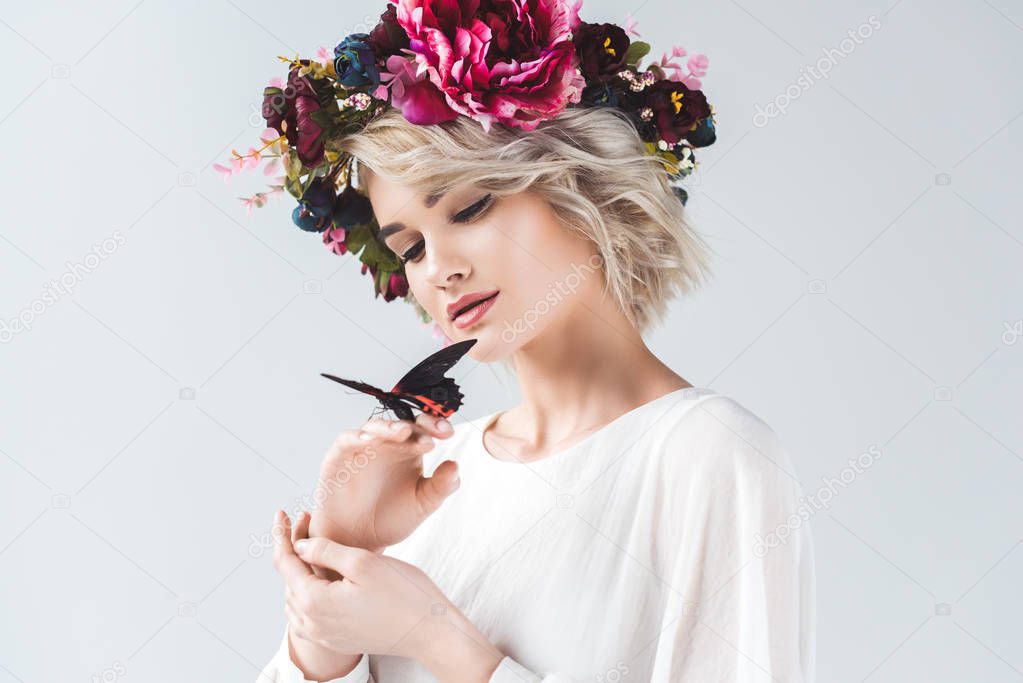 beautiful girl posing in fashionable wreath with butterfly on hands, isolated on grey