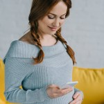 Attractive pregnant woman using smartphone in living room