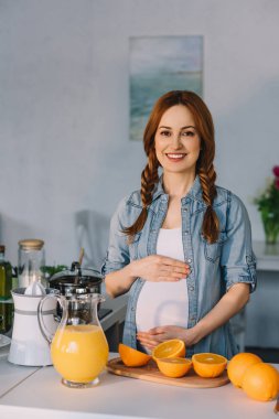 göbek dokunmaktan ve mutfak kameraya bakarak gülümseyen hamile kadın