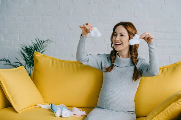 Happy Pregnant Woman Holding Newborn Shoes Looking Away Living Room — Stock Photo, Image