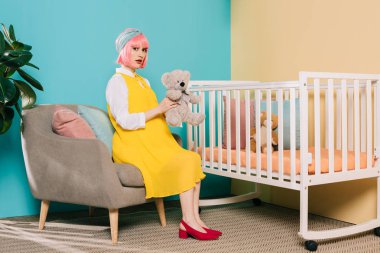 pembe saçlı çocuk odasında Bebek karyolası yakın oyuncak ayı ile oturan kadın hamile PIN Retro tarz