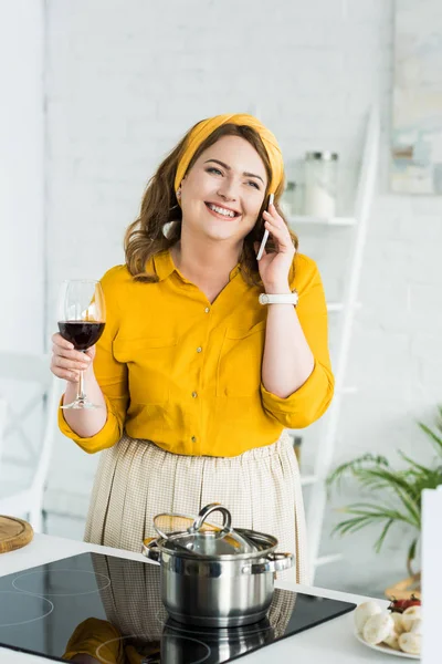 woman talking by smartphone and drinking wine in kitchen