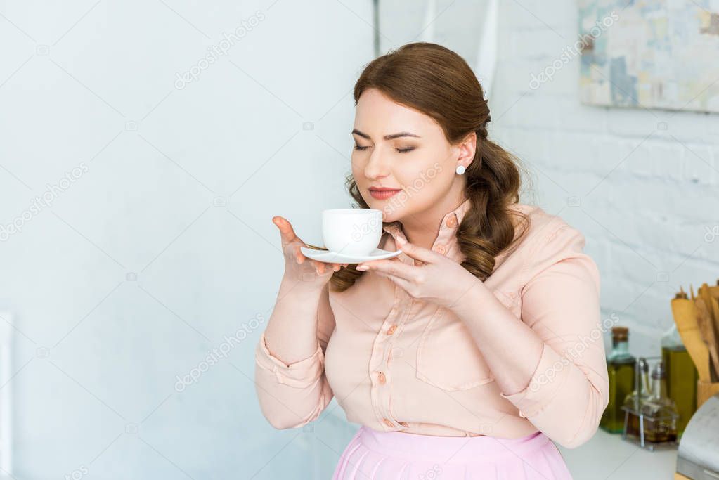 beautiful woman sniffing coffee with closed eyes in kitchen