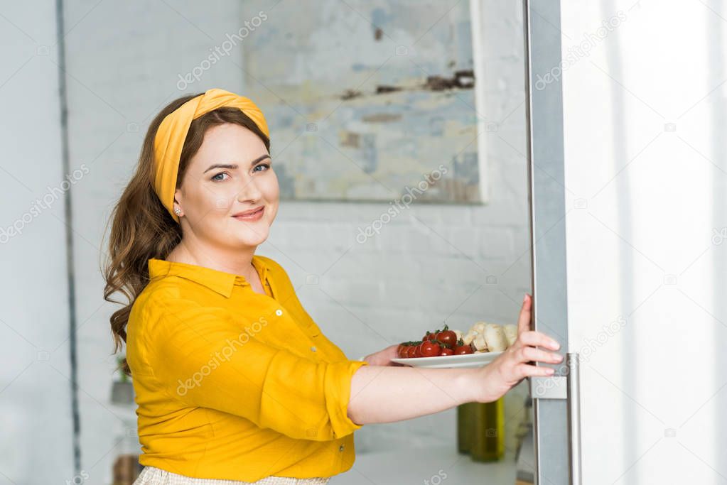 beautiful woman holding plate with vegetables at kitchen