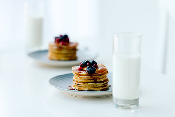selective focus of homemade pancakes with berries and honey and glasses of milk on tabletop