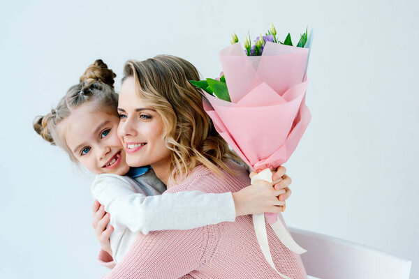 portrait of smiling daughter with bouquet of flowers and happy mother hugging each other, happy mothers day concept