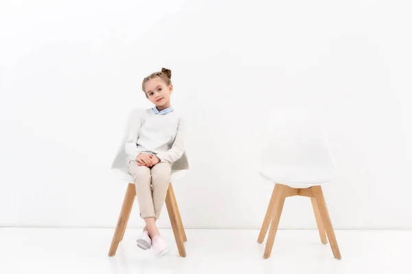 Entzückendes Kind Sitzt Auf Stuhl Und Blickt Kamera Auf Weiß — Stockfoto