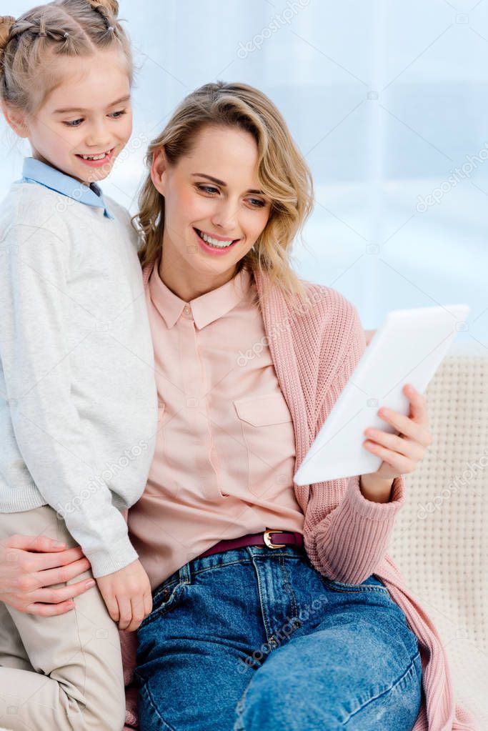 smiling mother and daughter looking at tablet at home