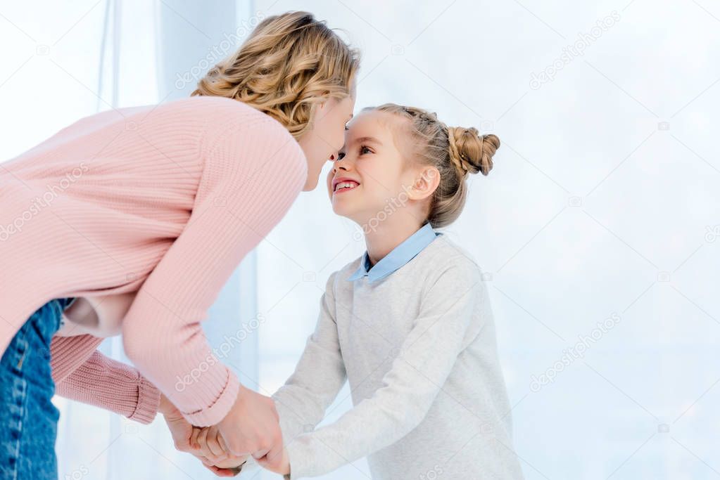 mother and daughter holding hands and touching with noses at home
