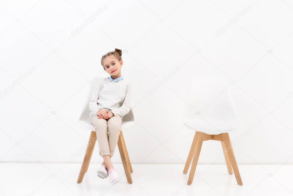 adorable child sitting on chair and looking at camera on white