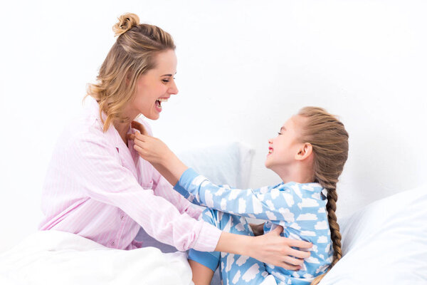 smiling mother tickling happy daughter on bed at home