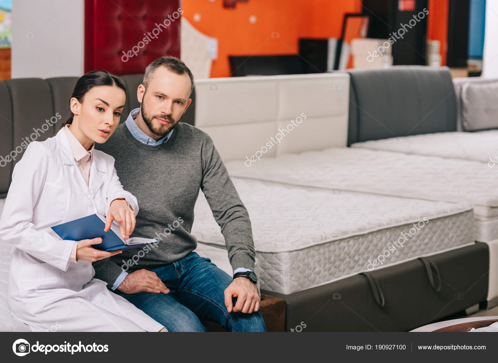 Female Shop Assistant White Coat Notebook Helping Customer Choosing Mattress ⬇ Stock Photo