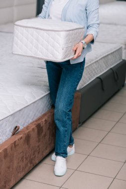 cropped shot of woman with folding mattress in hands in furniture shop clipart