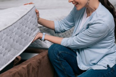 cropped shot of smiling woman choosing orthopedic mattress in furniture store clipart