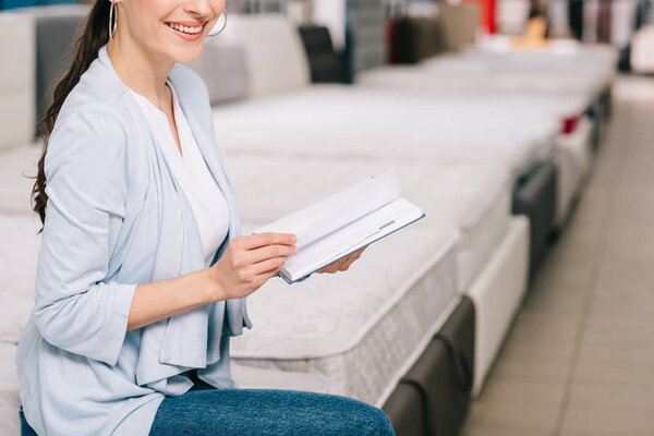 cropped shot of smiling female customer with notebook in furniture store with arranged mattresses