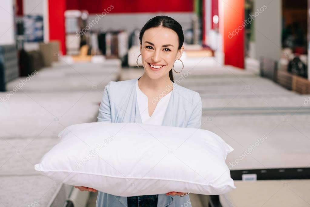 portrait of smiling woman holding pillow in furniture shop