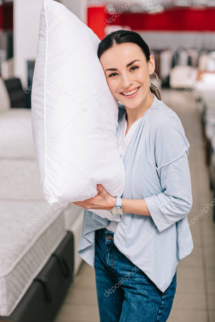 portrait of smiling woman holding pillow in furniture shop