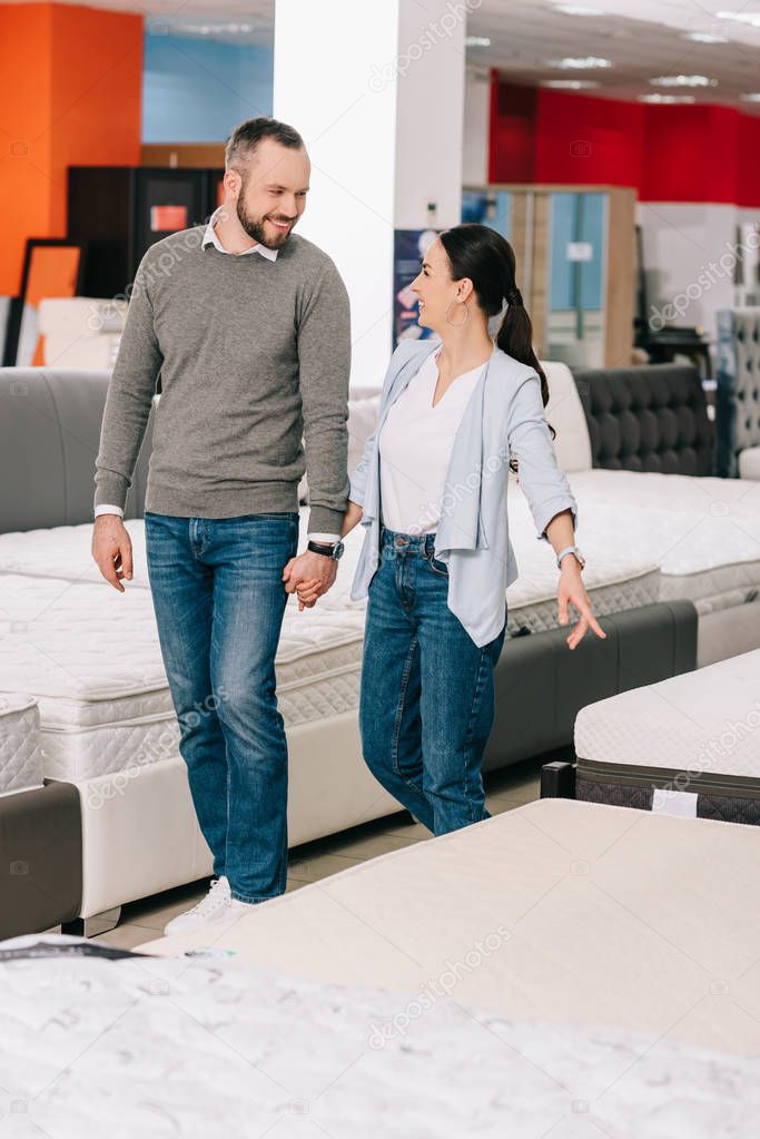 couple holding hands while choosing mattress together in furniture store