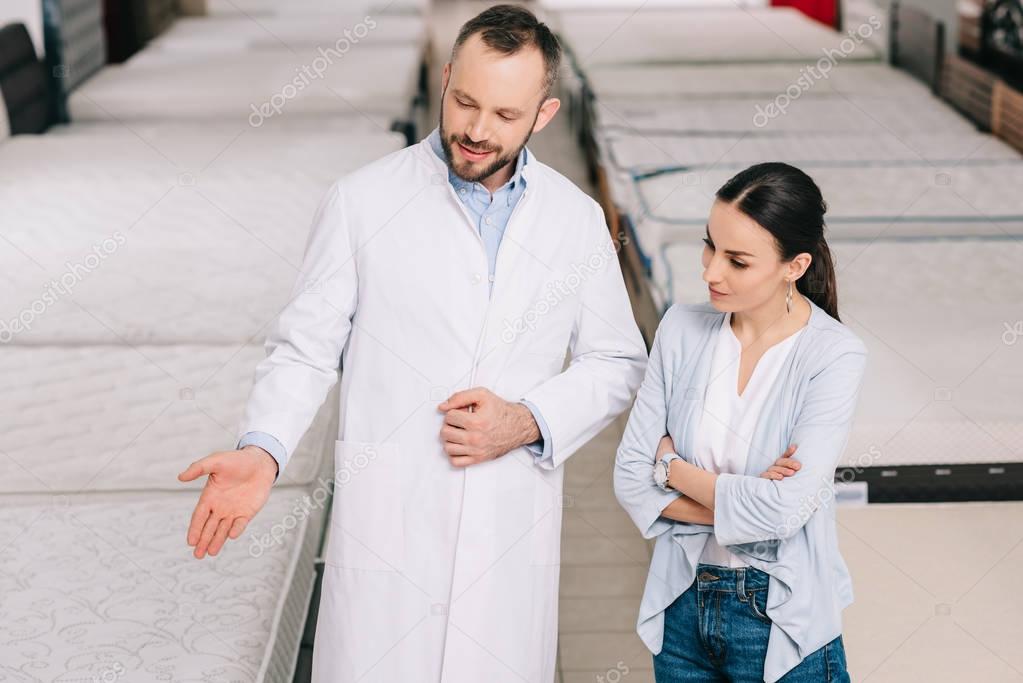 male shop assistant in white coat showing goods to customer in furniture shop