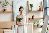 gyönyörű fiatal nő gazdaság cserepes növény és látszó-on fényképezőgép, művészeti stúdió