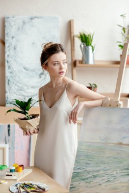 Yeşil güzel genç sanatçı şövale ve uzak Sanat stüdyosu arıyorsunuz resme eğilerek bitki saksı