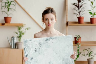 beautiful young naked artist holding picture and looking at camera clipart