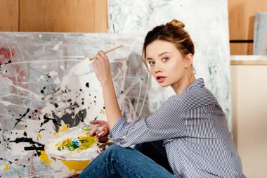 Palet tutarak ve Sanat Atölyesi kamerada bakarak güzel genç sanatçı