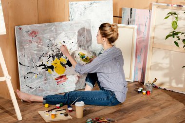 beautiful young female painter sitting on floor and drawing picture in art studio